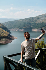 A young male tourist takes a selfie using his phone while standing in a natural location - observation deck near the canyon of the Uvac River, western Serbia. Travel Blogger guy outdoor.