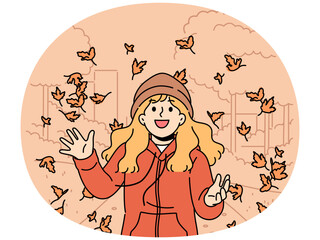 Little girl throws up leaves of autumn trees walking in park and rejoices at end of summer and onset of september. Happy child in autumn jacket and hat laughs standing among falling maple foliage
