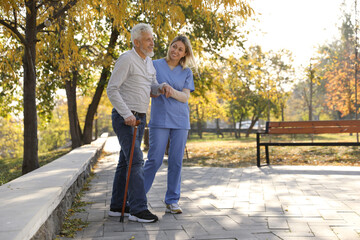 Caregiver assisting senior man in park, space for text. Home health care service