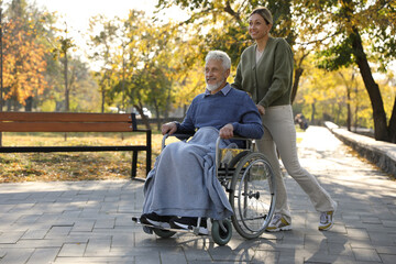 Caregiver assisting senior man on wheelchair in park, space for text. Home health care service
