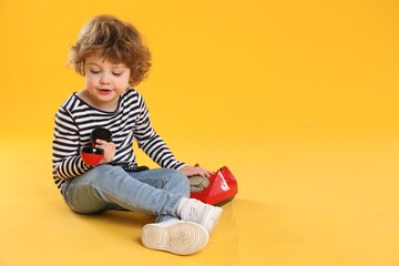 Naklejka premium Cute little boy with telephone on orange background, space for text