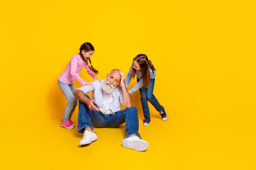 Grandfather playing with two young granddaughters in casual outfits against bright yellow backdrop in a fun family moment