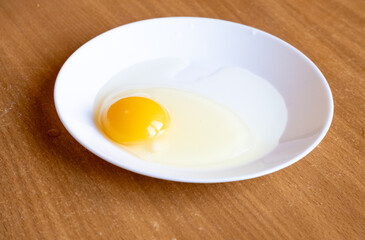 Raw egg in a white plate on the table.
