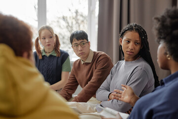 Multiethnic group of teenage children listening to female therapist during support session in...