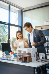 A businessman and woman sit at a table, discussing a two-story house for sale in a village project. They focus on property details, real estate opportunities, and housing investments