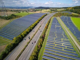 Aerial view of solar panels located along a highway, with a landscape of green fields and hills....