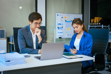 A businessman and woman sit at a modern office table, smiling and discussing a new project or business startup. They collaborate with a laptop, focusing on strategic planning and teamwork