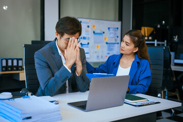 A stressed businessman and woman sit at a desk, overwhelmed by business challenges. They discuss problems,financial pressures, and strategy, seeking solutions to manage work, deadlines, and economic