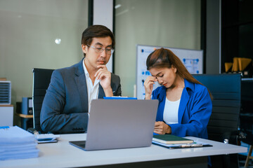 Obraz premium A stressed businessman and woman sit at a desk, overwhelmed by business challenges. They discuss problems,financial pressures, and strategy, seeking solutions to manage work, deadlines, and economic