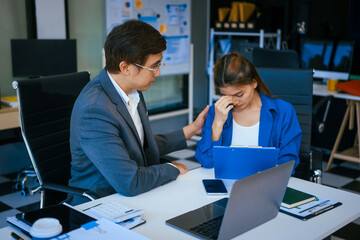A stressed businessman and woman sit at a desk, overwhelmed by business challenges. They discuss problems,financial pressures, and strategy, seeking solutions to manage work, deadlines, and economic