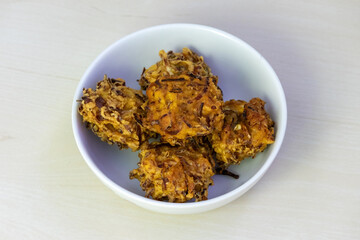 Crispy, crunchy pakora served on a white bowl. These delicious deep-fried fritters are a popular snack or appetizer in Bangladesh, India, and other parts of South Asia.