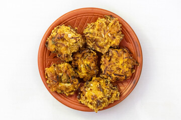 Crispy pakora on a clay plate, isolated on a white background. These delicious, deep-fried fritters are a popular snack or appetizer in Bangladesh, India, and other parts of South Asia. Top view.