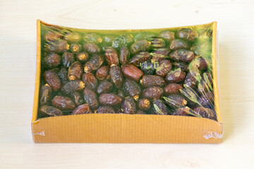 Dried date palm fruits are contained within a cardboard box, resting on a wooden surface. Dates are a popular fruit consumed during the Islamic holy month of Ramadan.