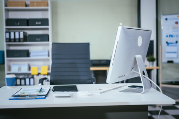 An empty desk with a computer displaying a graph on the screen, a tablet placed on the table, and a chair positioned near. The workspace is neat and ready for use