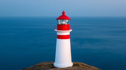 Red and white lighthouse on a cliff overlooking a calm blue ocean.