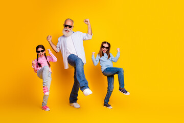 Joyful grandfather dancing with his granddaughters on a vibrant yellow backdrop