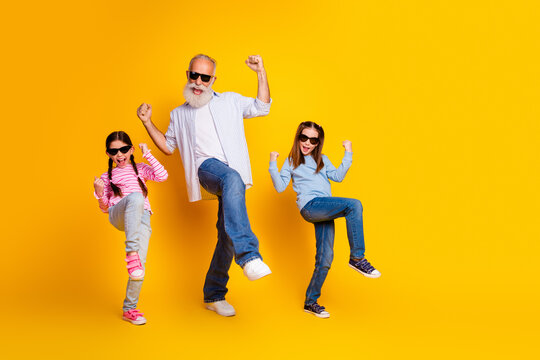 Joyful grandfather dancing with his granddaughters on a vibrant yellow backdrop