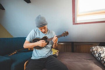 Musician with smile sits on a cozy bed, strumming a black ukulele. Enjoying the feeling of playing...