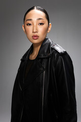 Fototapeta premium Fashion asian woman in black leather jacket posing for studio portrait on gray background