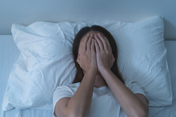 Stressed can not sleep asian young woman, girl use hand to cover her face on bed at home, suffering...