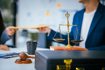 A male and female lawyer are sitting at a desk in an office, discussing legal documents and...
