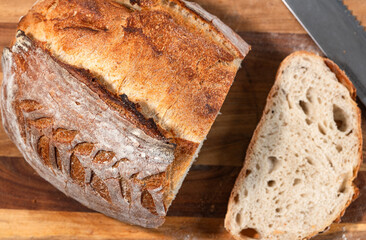 A close-up overhead image showcases a sliced homemade loaf of bread on a wooden surface, accompanied by a single slice and a bread knife.