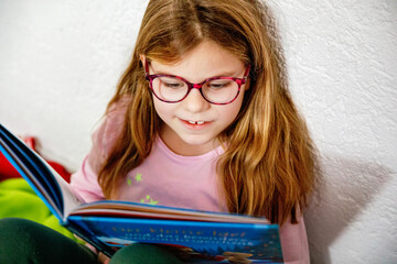 Little girl with eyeglasses reading book. Happy interested child learning.