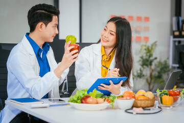 Two nutritionists,female and male, work in a hospital, analyzing vegetable and fruit salads,...