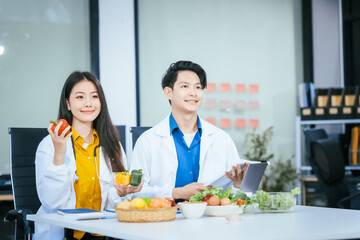 Two nutritionists,female and male, work in a hospital, analyzing vegetable and fruit salads, offering online advice, helping patients embrace clean eating habits and weight control for better health