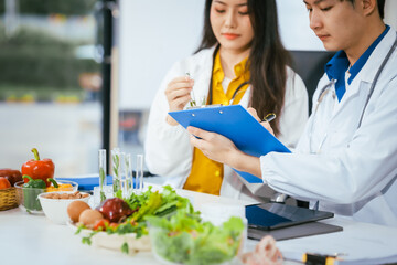 Two nutritionists,female and male, work in a hospital, analyzing vegetable and fruit salads, offering online advice, helping patients embrace clean eating habits and weight control for better health