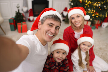 Fototapeta premium Happy family taking selfie together in Santa hats at home. Christmas season