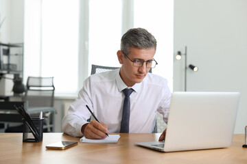 Naklejka premium Middle aged man working with laptop at table in office