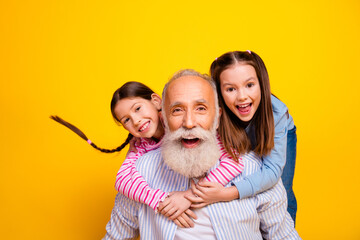 Smiling grandfather with cheerful granddaughters having fun together against a bright yellow background depicting happiness and family bonding