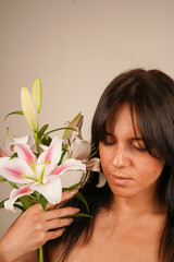 A serene moment as a dark-haired woman with closed eyes holds lilies on her shoulder. The pastel...