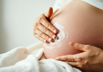Expecting mother applying lotion on her belly in a cozy indoor setting during daytime