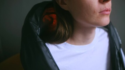 Relaxed woman massages neck with heat vibrating device dealing with pain at home. Electric equipment for physical injury treatment usage