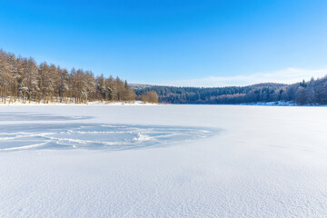 Obraz premium Serene Winter Landscape with Snow Covered Lake and Trees Under Clear Blue Sky