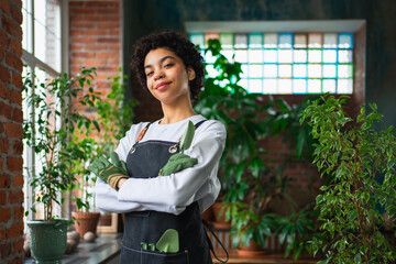 Running of own business. African woman florist wearing apron in botanical store with green plants. Happy small business owner working at flower shop smiling surrounded by plants Small business