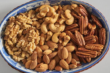 Assorted nuts in a stoneware container with a straw basket, on a white background. Almonds, Walnuts, Cashews and Chestnuts