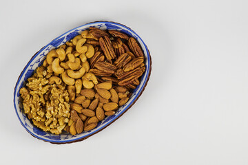 Assorted nuts in a stoneware container with a straw basket, on a white background. Almonds, Walnuts, Cashews and Chestnuts