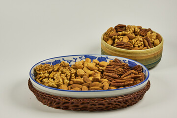 Assorted nuts in a stoneware container with a straw basket, on a white background. Almonds, Walnuts, Cashews and Chestnuts