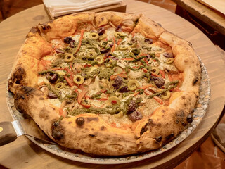 Artisanal pizza with meats, vegetables of various types and mozzarella cheese served on a colorful plate on a wooden table