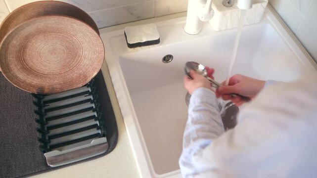 Woman engages in washing up dishes after dinner in modern kitchen. Housewife hands put spoons onto dish drying rack placed on countertop