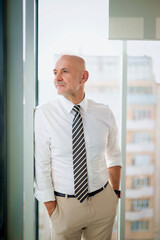 Fototapeta premium Mid aged man standing by the window and looking thoughtful