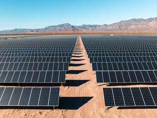 Aerial view of vast solar farm in desert landscape with mountains on a sunny day. © Nick