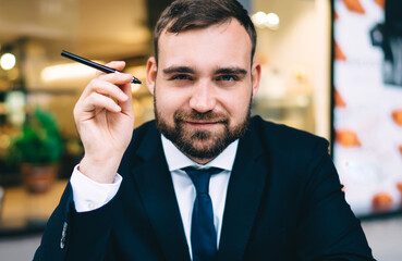 Half length portrait of formally dressed businessman 30s sitting at sidewalk table in street cafe...