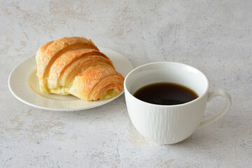 a cup of black coffee and a croissant on the white saucer