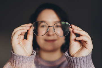 Happy young woman holding eyeglasses in hands, close up.