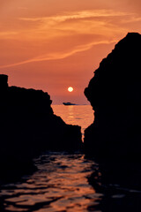Sun setting over rocks on a beach, reflecting in the water