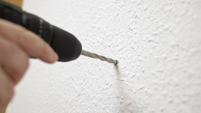 close-up of drilling a white wall using an electric drill with a drill bit. Focus on the drill. construction, renovation, DIY projects, advertising of construction tools, training.